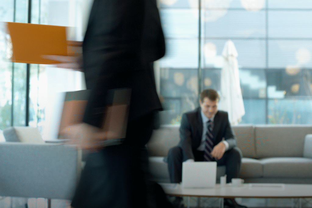 Texto alternativo de imagen: Ambiente laboral que hace percibir que hay incertidumbre, una persona camina de forma borrosa mientras que al fondo hay un hombre consultando su computador portátil