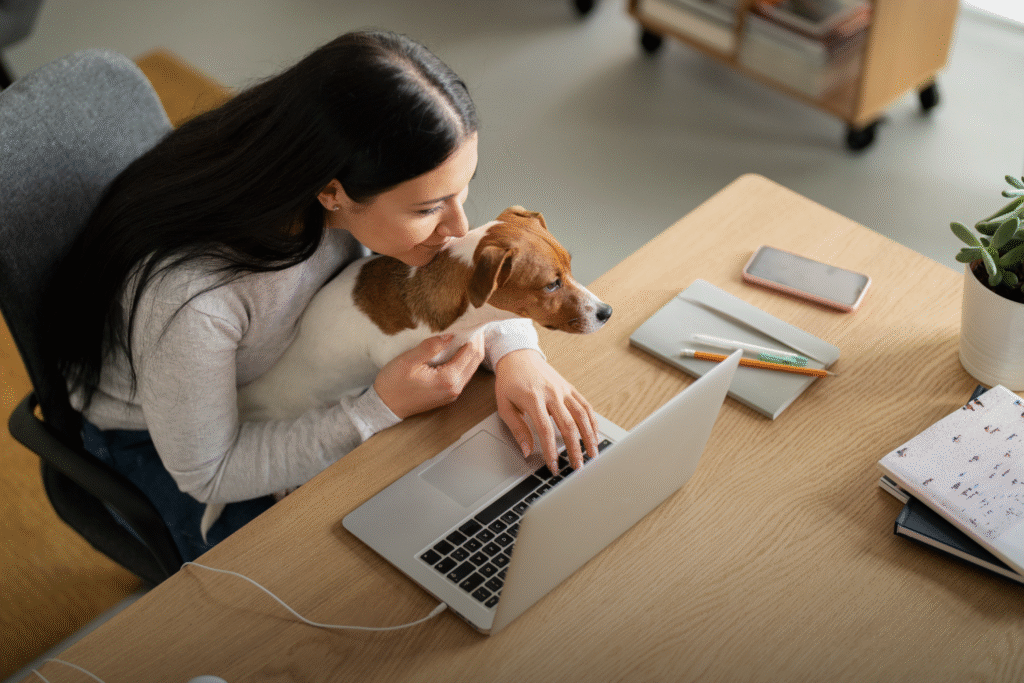 Una mujer haciendo teletrabajo, mientras sostiene a su mascota. Se encuentra en un lugar cómodo y adecuado para ella.